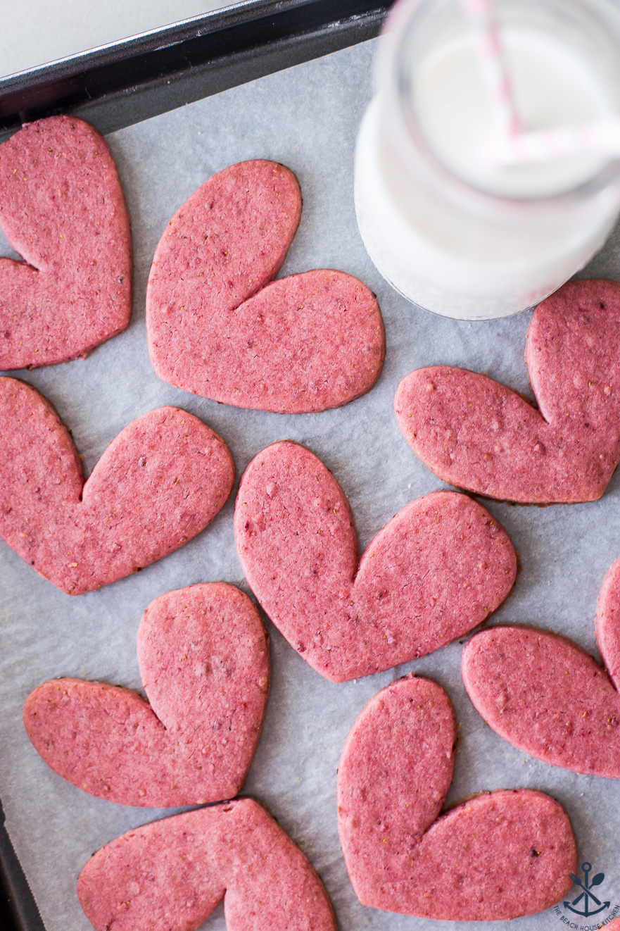 Overhead photo of pink heart shaped cookies on a tray with a bottle of milk with two straws