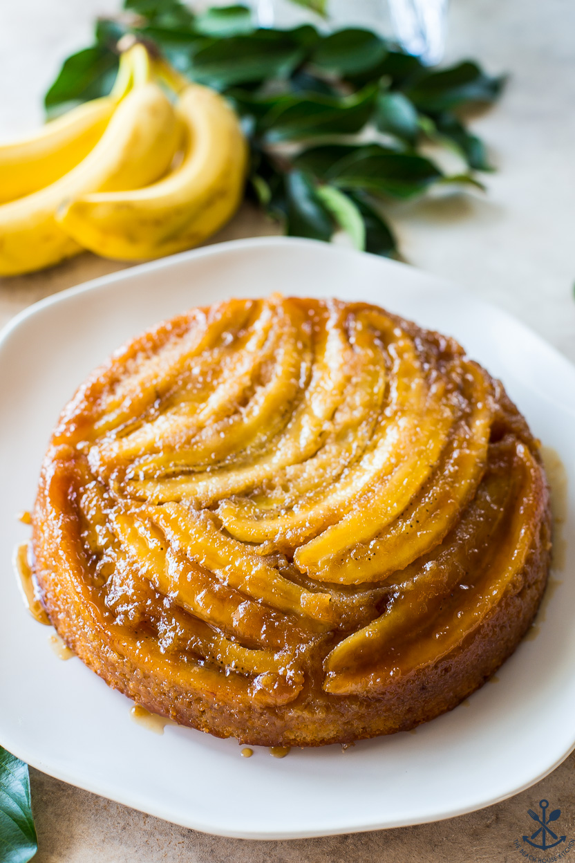 Caramelized Banana Upside-Down Cake on a white round plate with bananas in the background