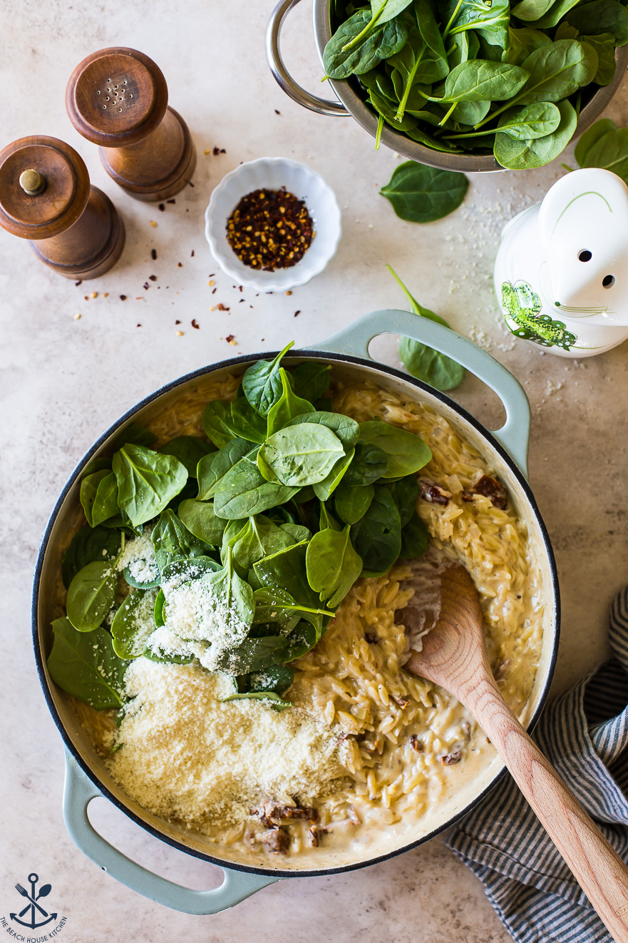 Overhead photo of a skillet of cooked orzo topped with spinach leaves