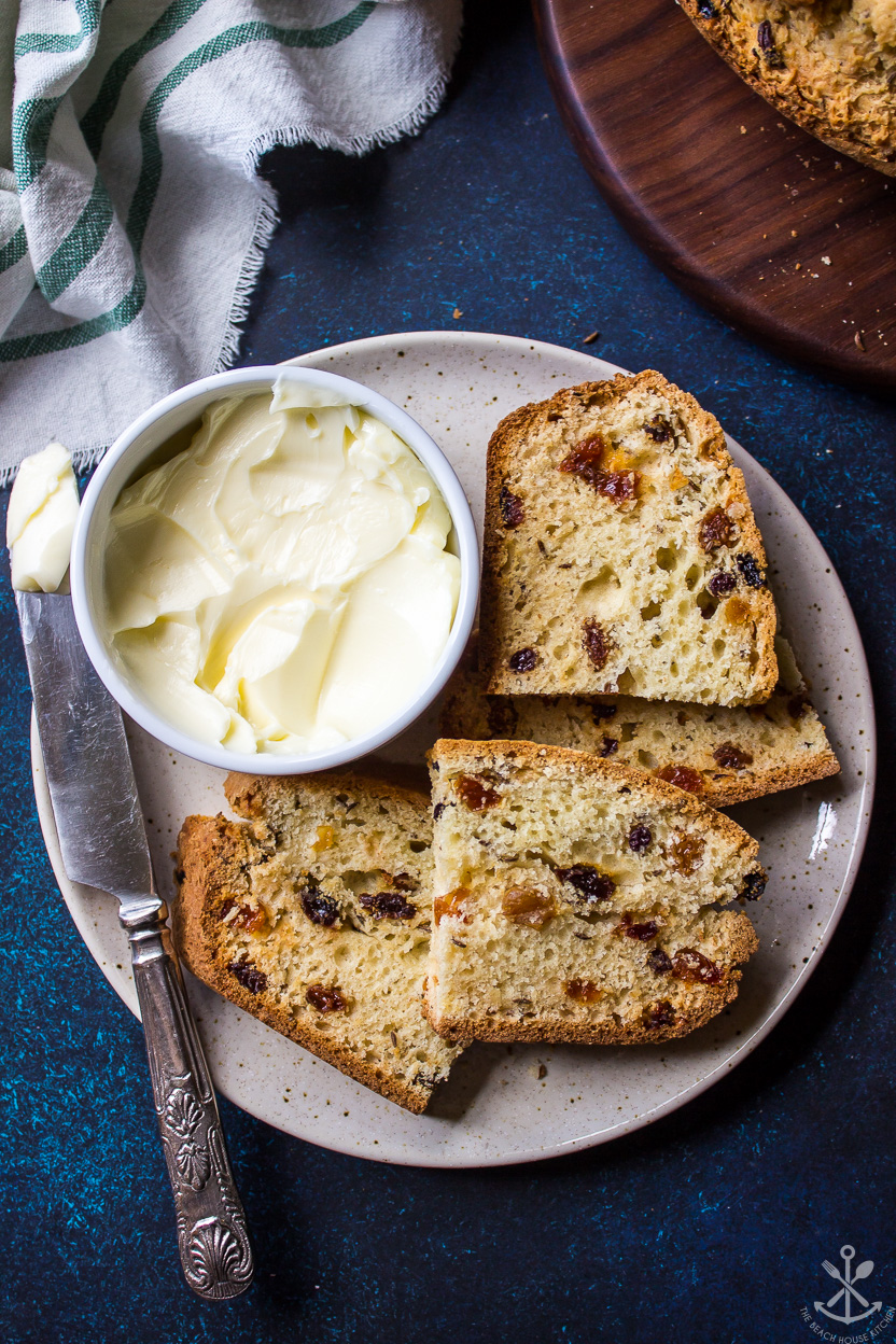 Up close overhead photo of slices of bread with raisins on a plate with a bowl of butter and a knife