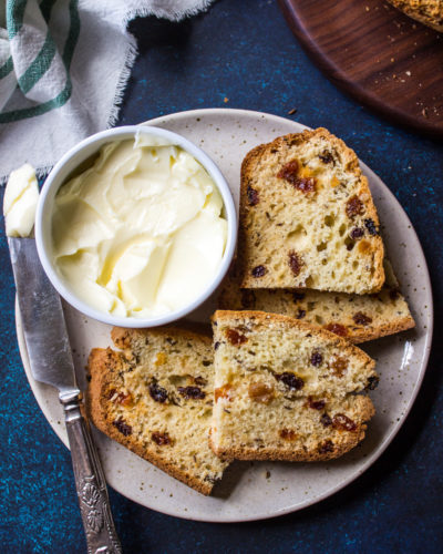 Overhead up close photo of slices of Irish Soda Bread on a plate with a bowl of butter and a knife