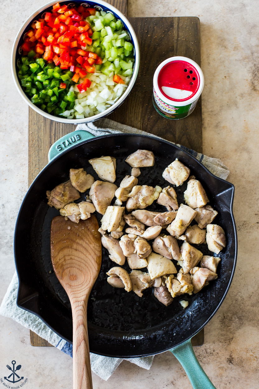 Overhead photo of a skillet of cooked chicken with a cowl of onions, peppers and celery off to the side