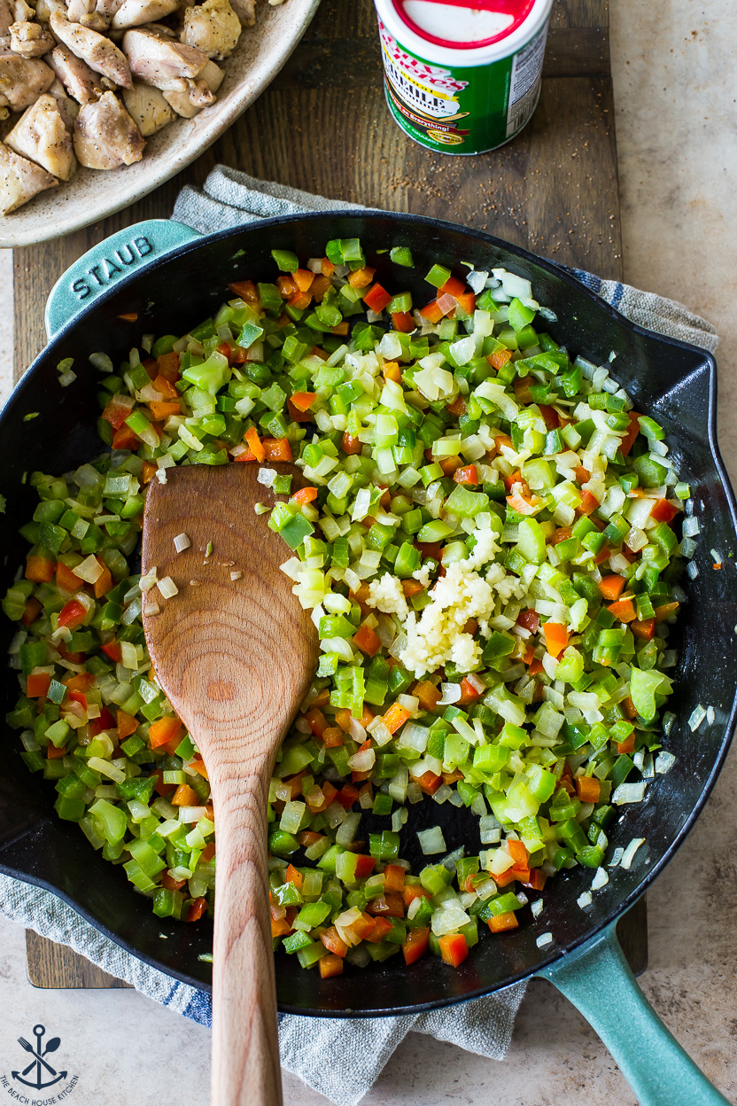 Up close overhead photo of a skillet of veggies and minced garlic with a wooden spoon
