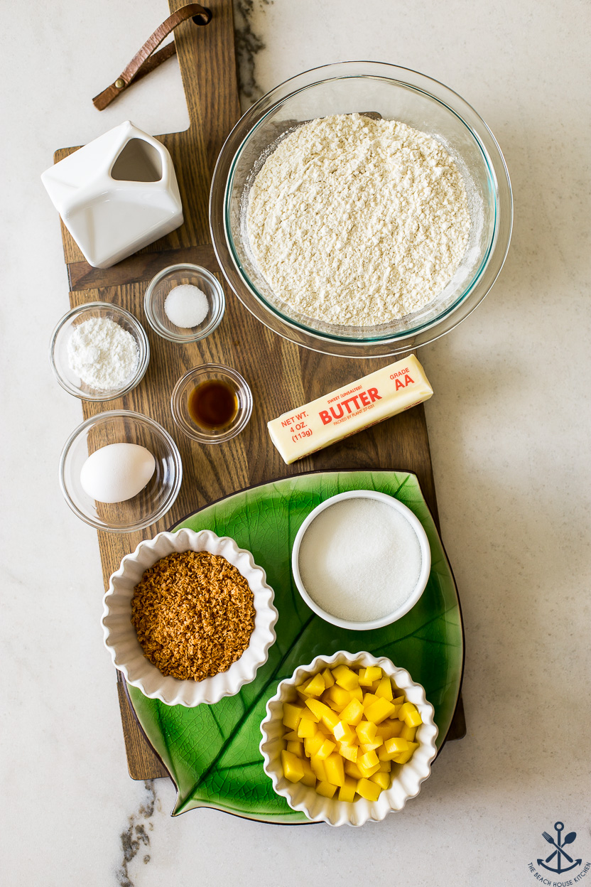 Overhead photo of ingredients for limed glazed mango toasted coconut scones on a wooden board in bowls