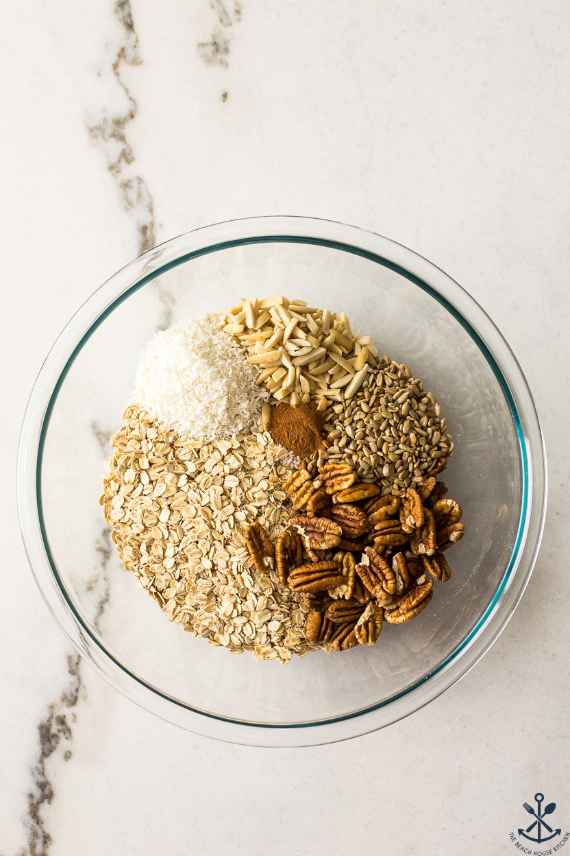 Overhead photo of a glass bowl filled with oats, nuts, coconut, sunflower seeds and cinnamon