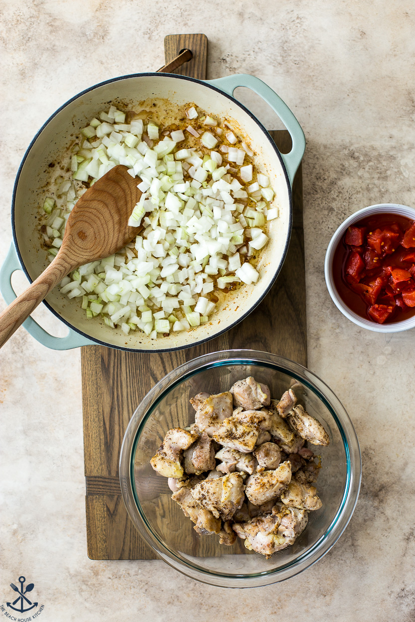 Overhead photo of a skillet of pre-cooked chopped onions, a bowl of chopped tomatoes and a bowl of cooked chicken pieces