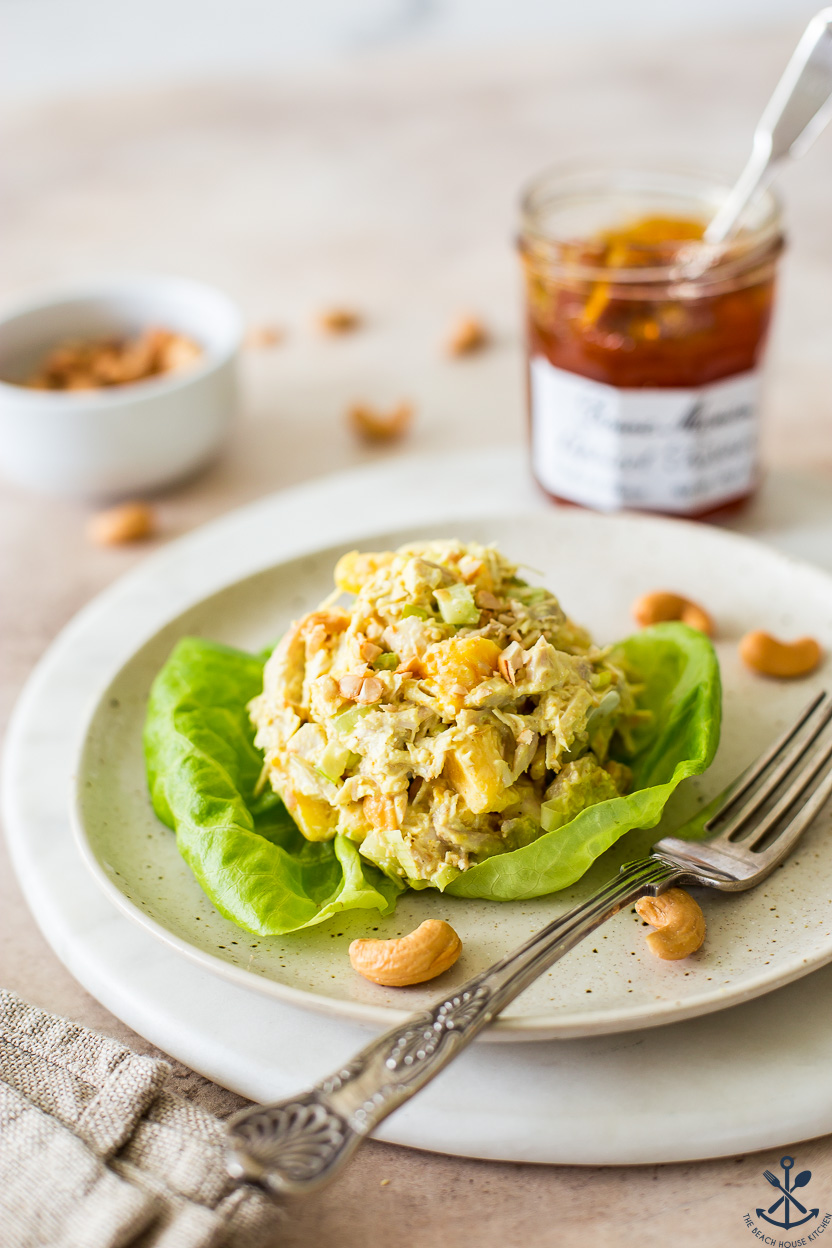 Chicken salad on a piece of lettuce on a plate with a fork and a jar of preserves in the background