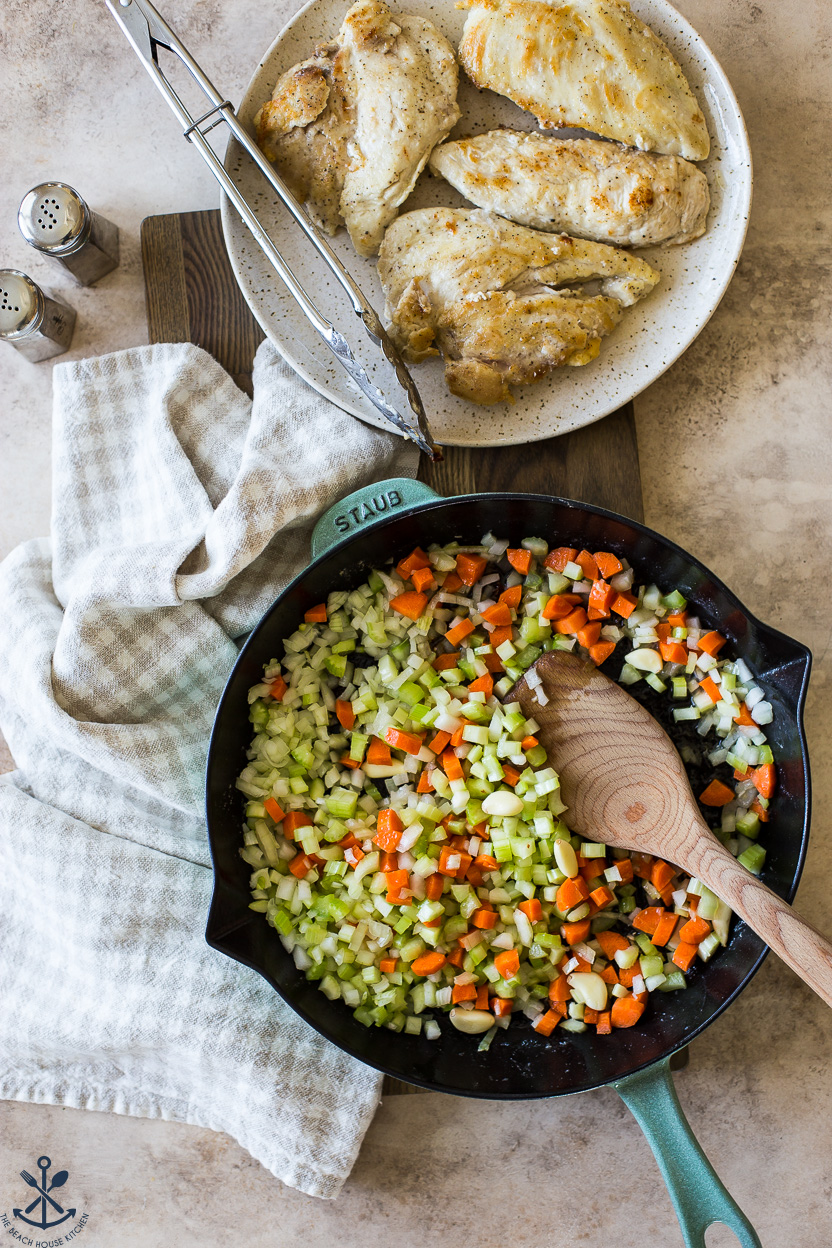 Overhead photo of a skillet filled with veggies and a plate of lightly browned chicken breasts