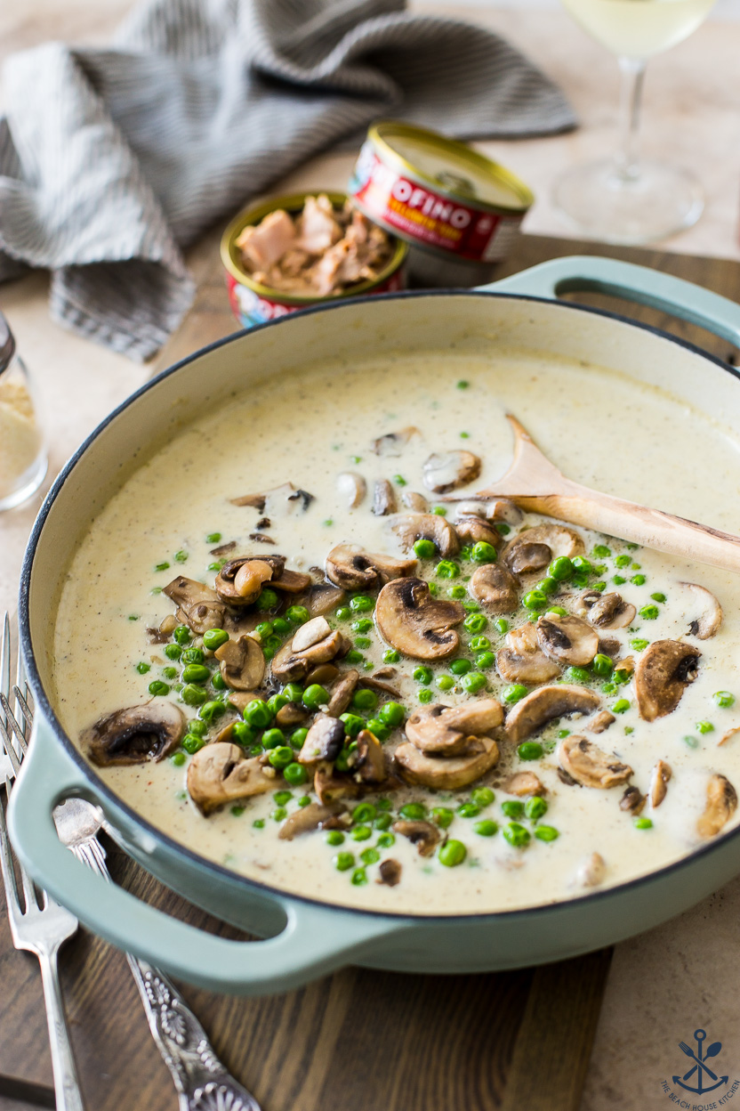 A skillet filled with a cream sauce with mushrooms and peas