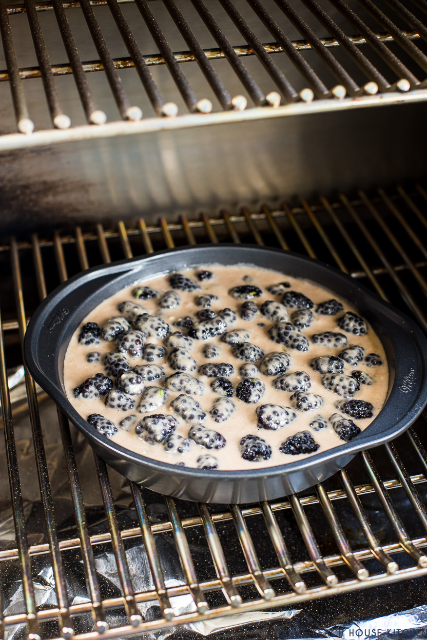 A baking pan fill with blackberries and biscuit batter on a grill