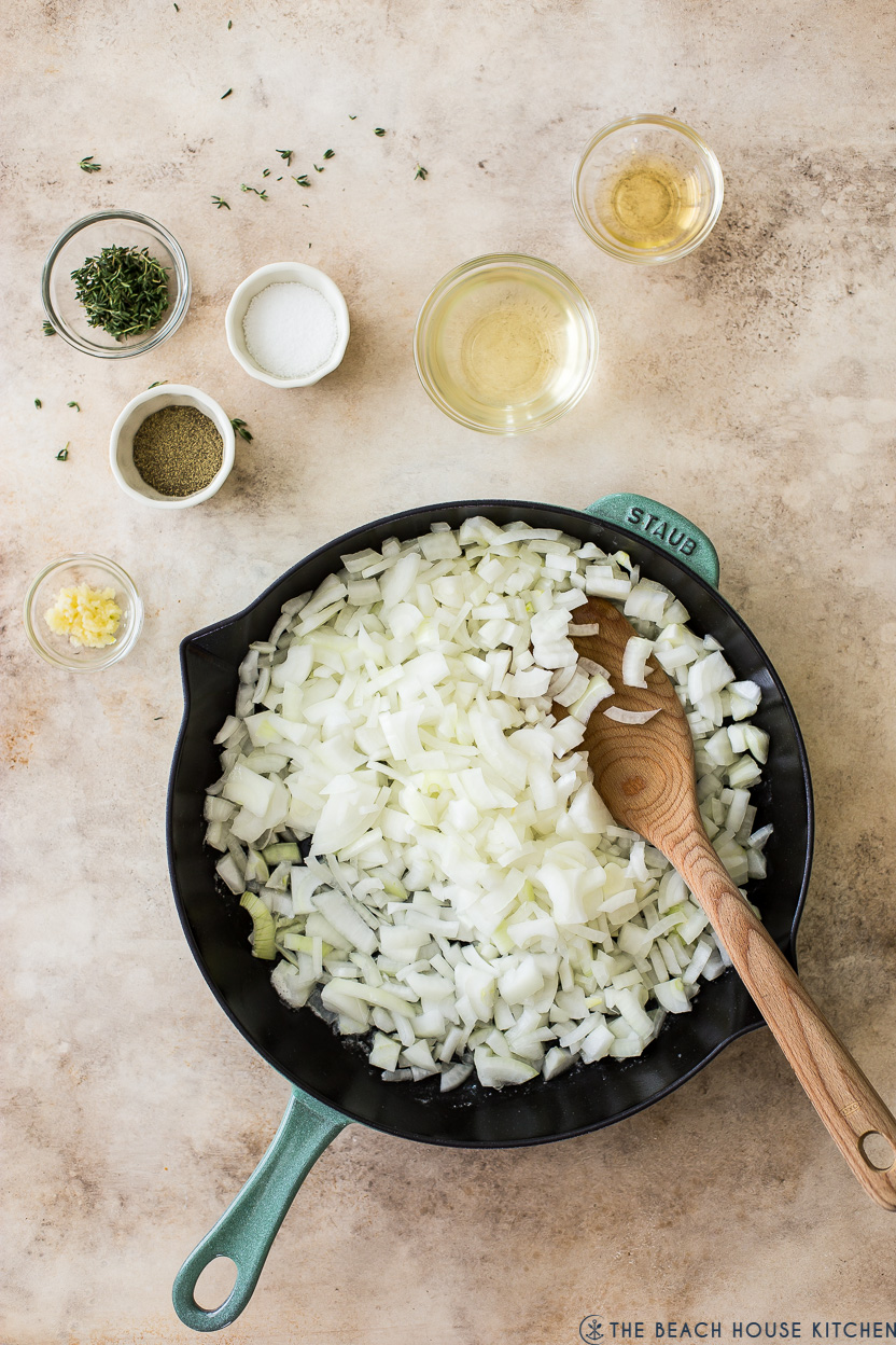 Overhead photo of a skillet of chopped onions with a few small bowls of spices 