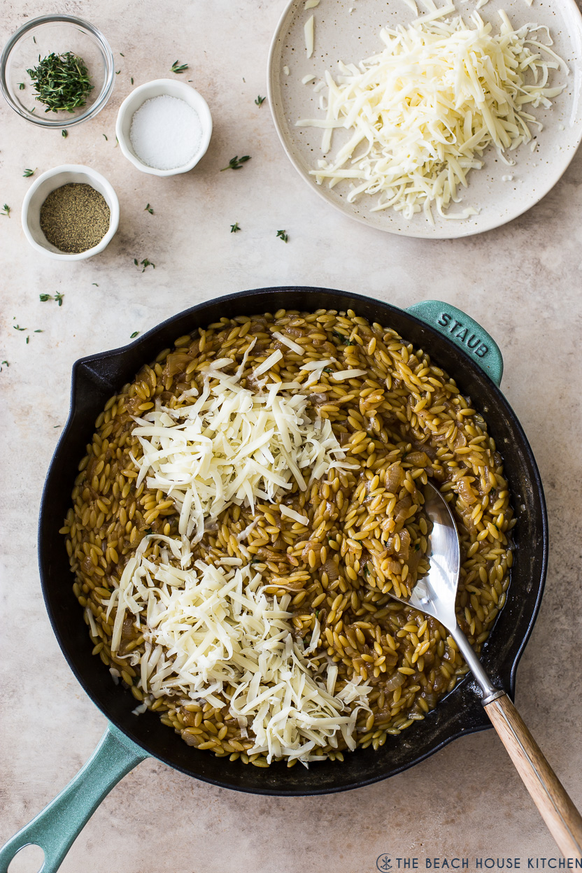 Overhead photo of a skillet or orzo topped with shredded gruyere cheese