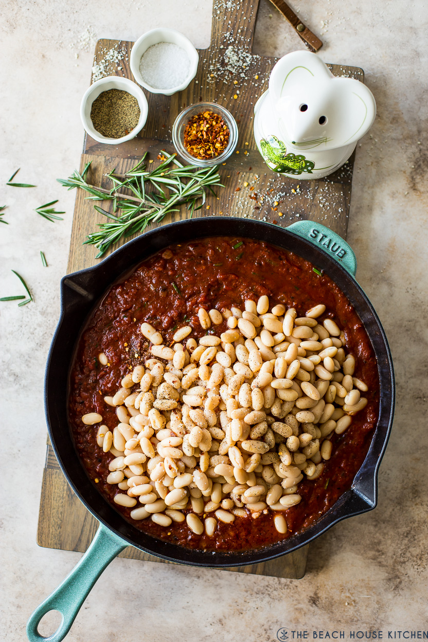 Overhead photo of a skillet of crushed tomatoes topped with cannellini beans