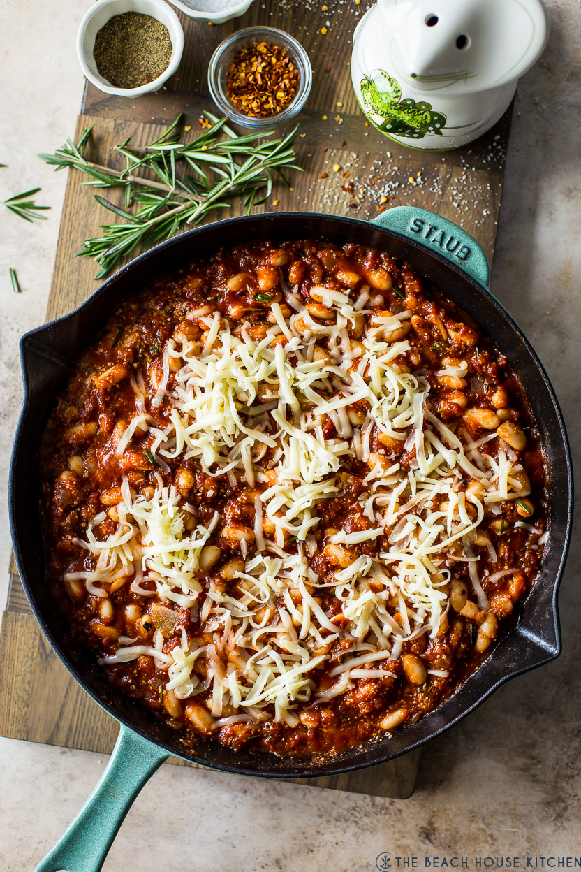 Overhead photo of a skillet of pre-baked Italian baked beans topped with shredded cheese