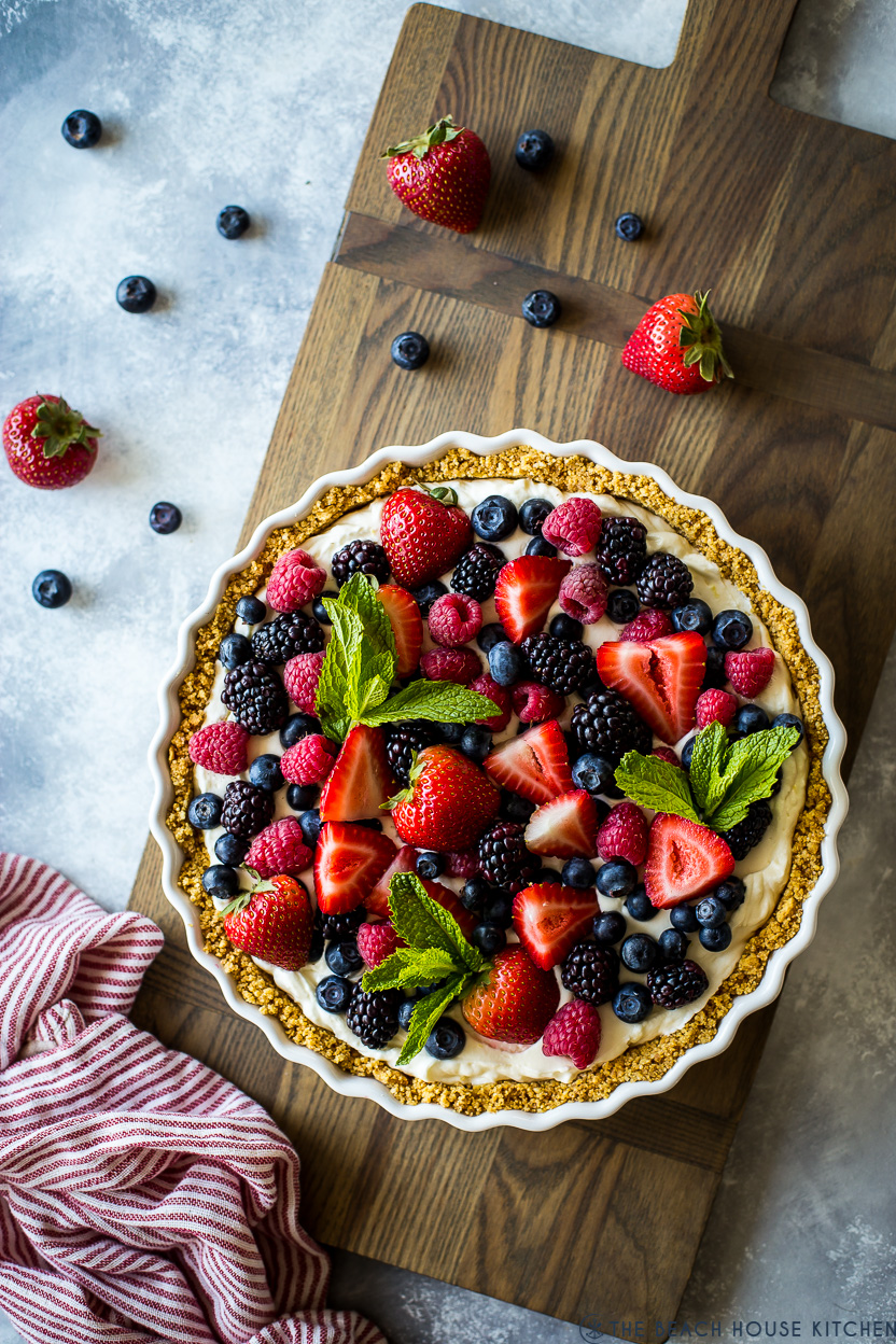 Overhead photo of a tart topped with fresh berries on a wooden board