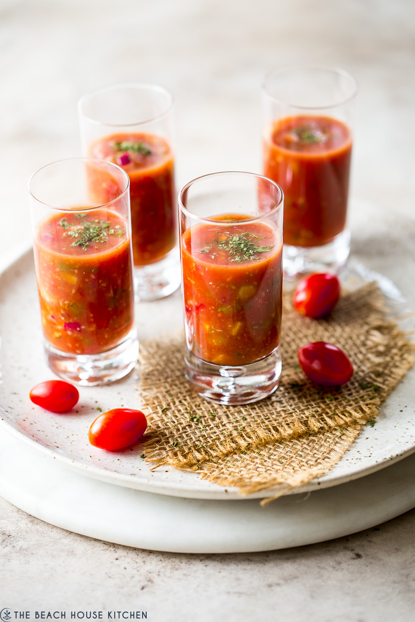 Four shooters glasses filled with gazpacho of a round marble board