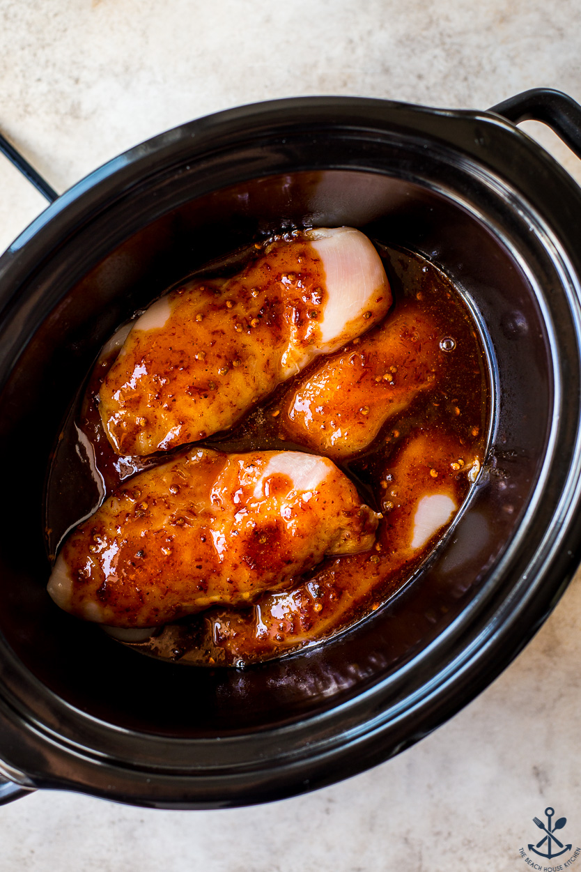 Overhead photo of pre-cooked chicken breasts covered with a chipotle sauce in a slow cooker