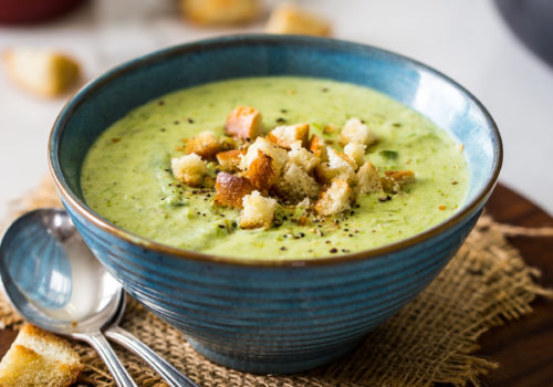 A bowl of smoky asparagus soup on a round wooden board with two spoons