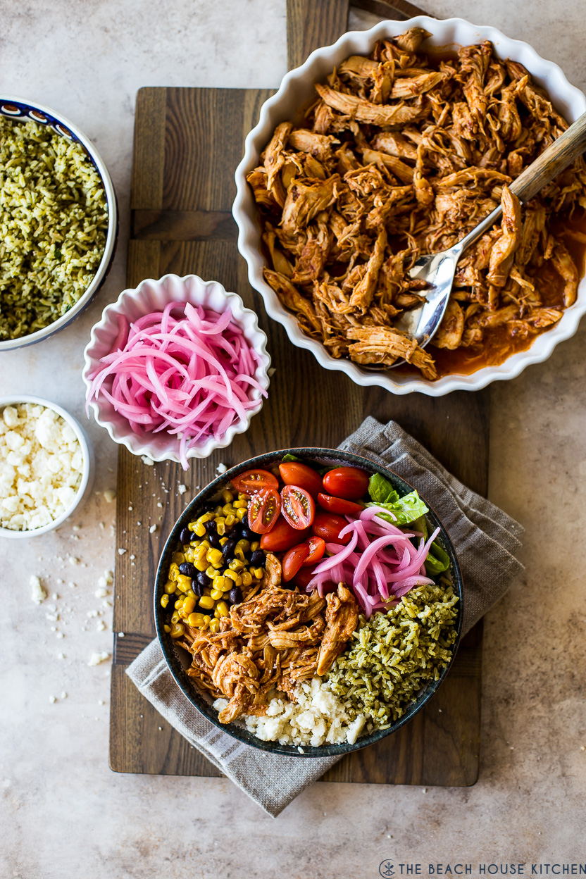Overhead photo of a honey chipotle chicken bowl, a dish of red onions, and a large dish of shredded chicken