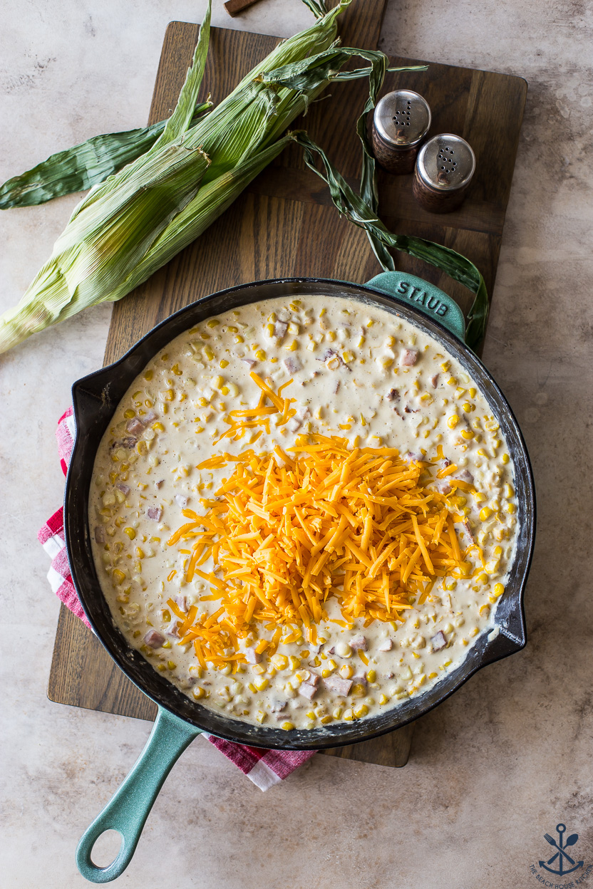 Overhead photo of a skillet of creamy corn topped with shredded yellow cheddar