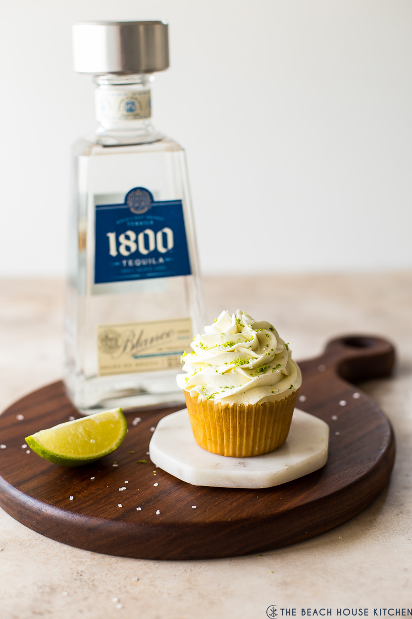 A margarita cupcake on a white marble coaster with a bottle of tequila in the background