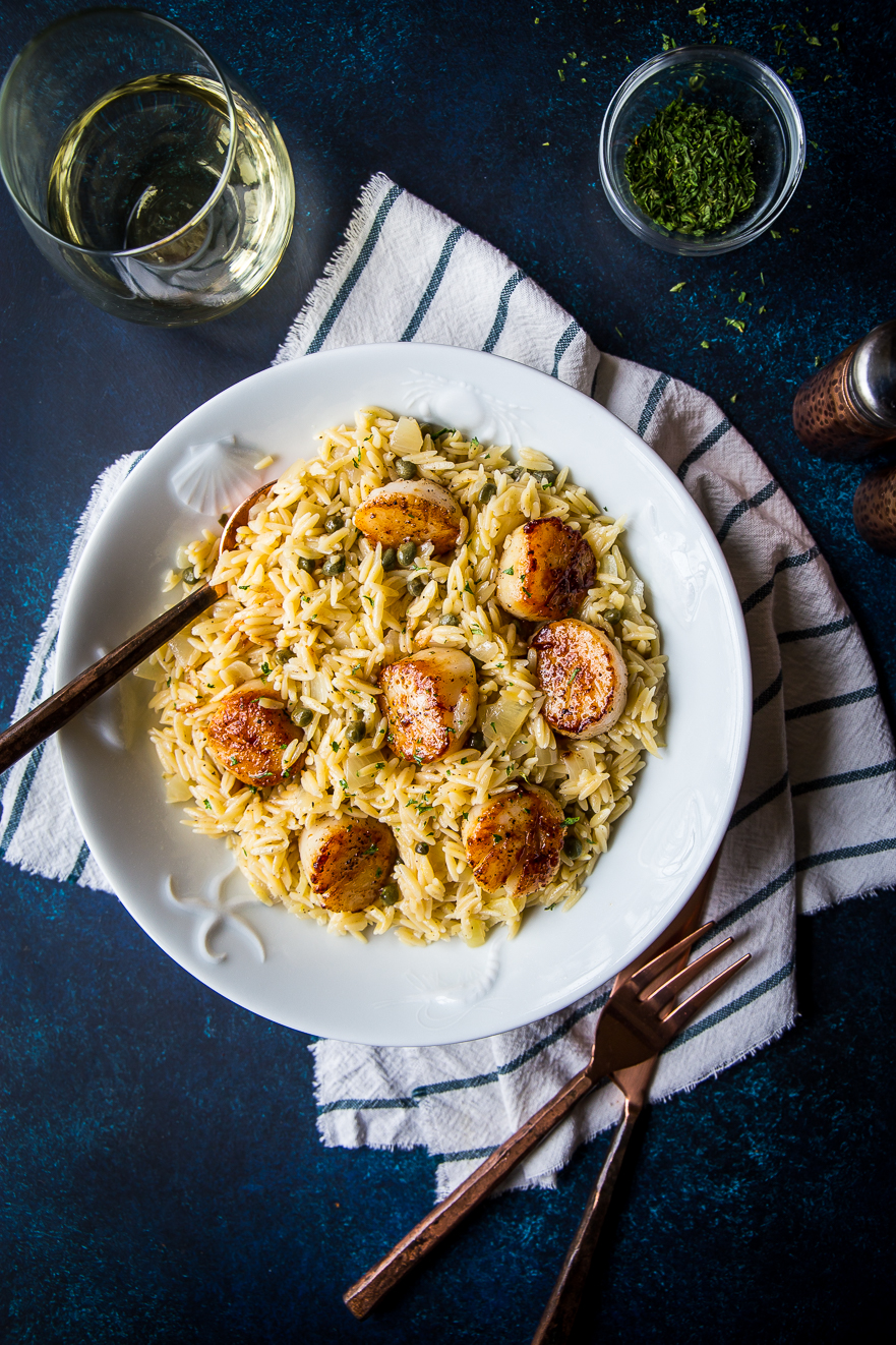 Overhead photo of a white bowl filled with scallops and orzo
