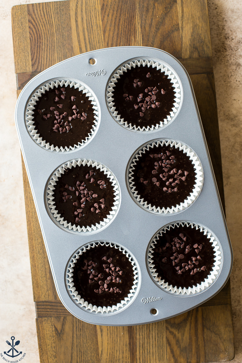 Overhead photo of pre-baked jumbo chocolate muffins in a muffin tin on a wooden board