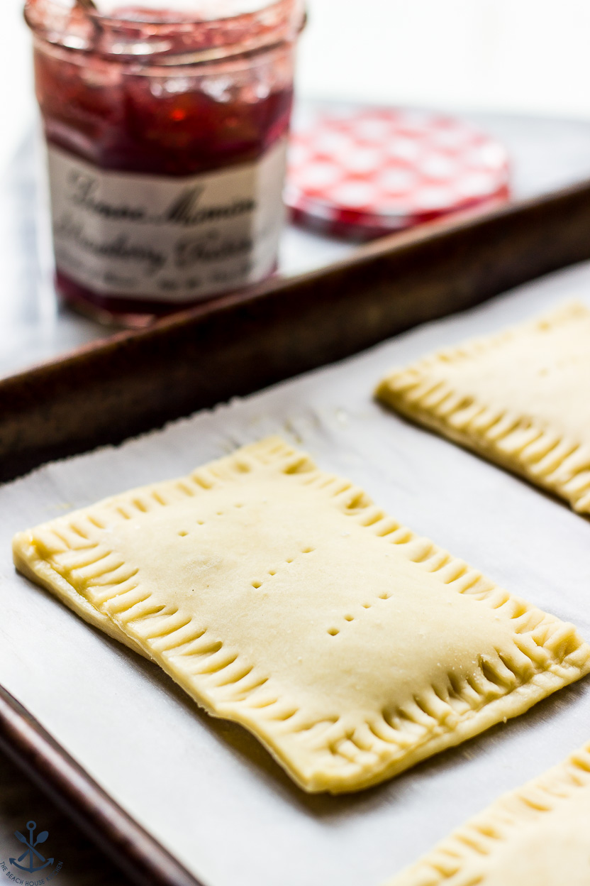 A pre-baked pop-tart on a parchment-lined baking sheet with a jar of jelly in the background