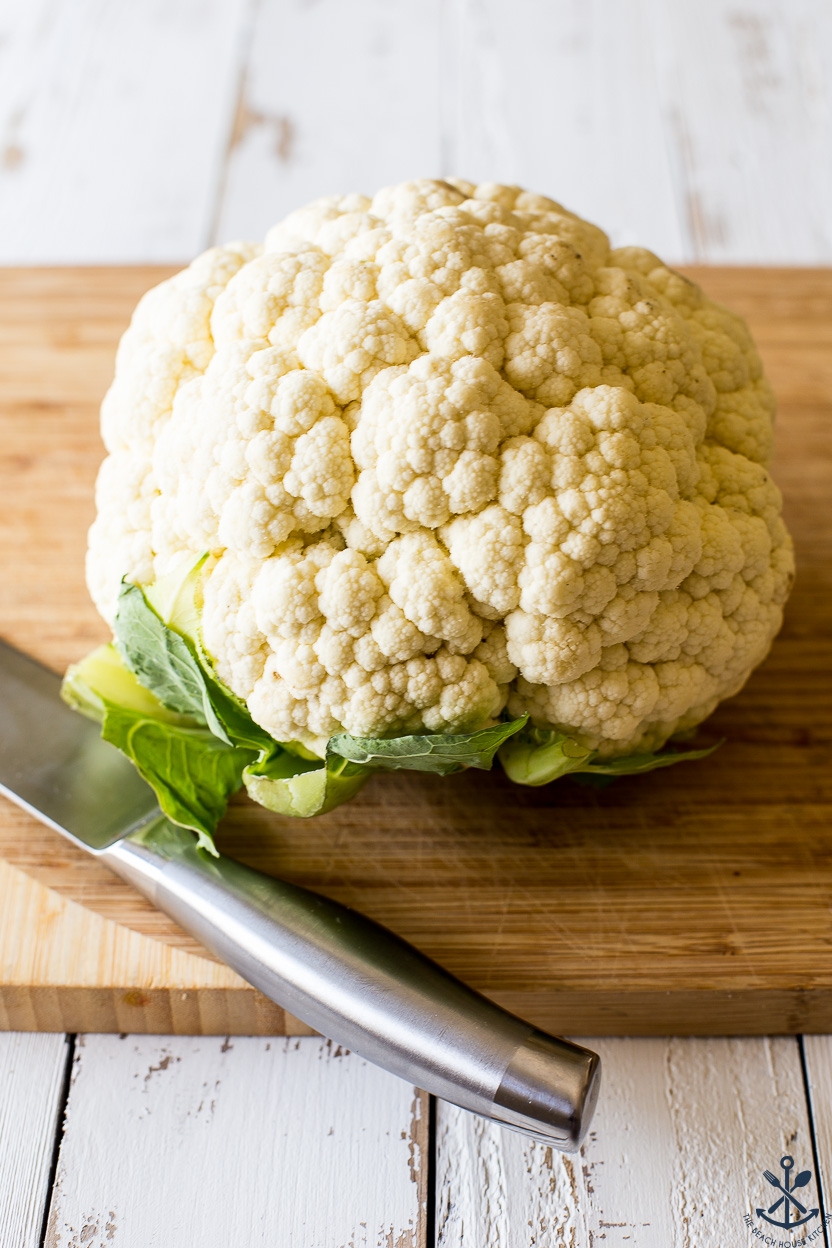 A head of cauliflower on a wooden board with a large silver knife