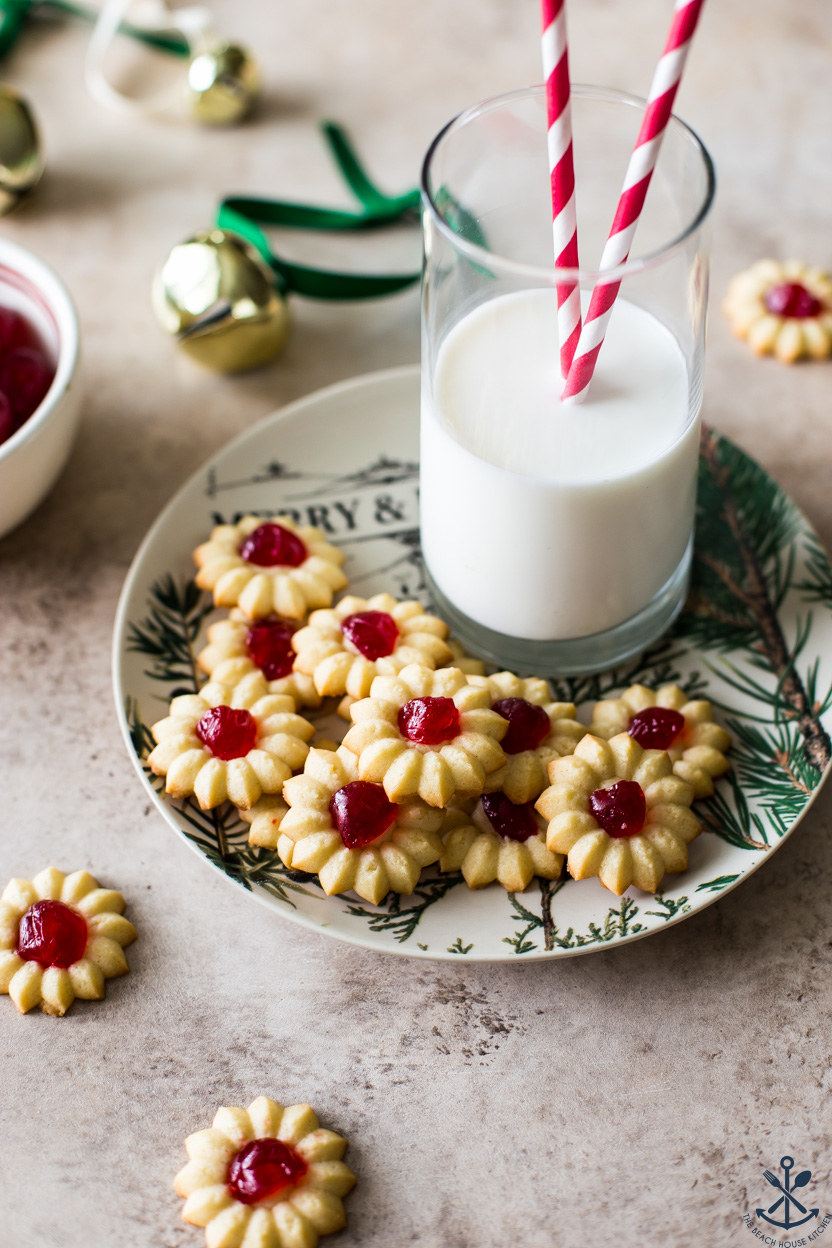 Cherry Almond Spritz cookies on a plate with a glass of milk with two straws