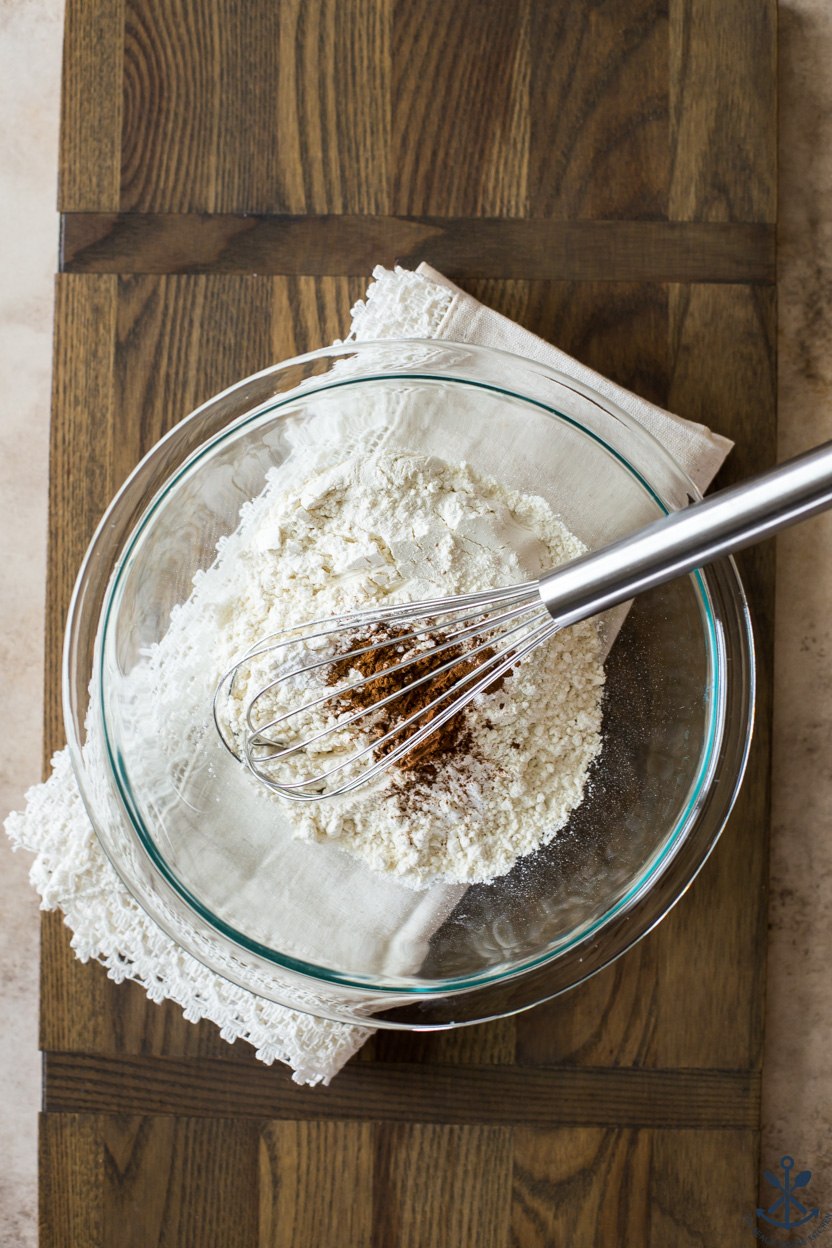 Overhead photo of a bowl of flour and cinnamon with a silver whisk