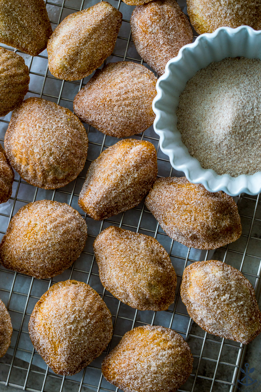 Overhead photos of madeleines on a wire rack with a white bowl of cinnamon sugar