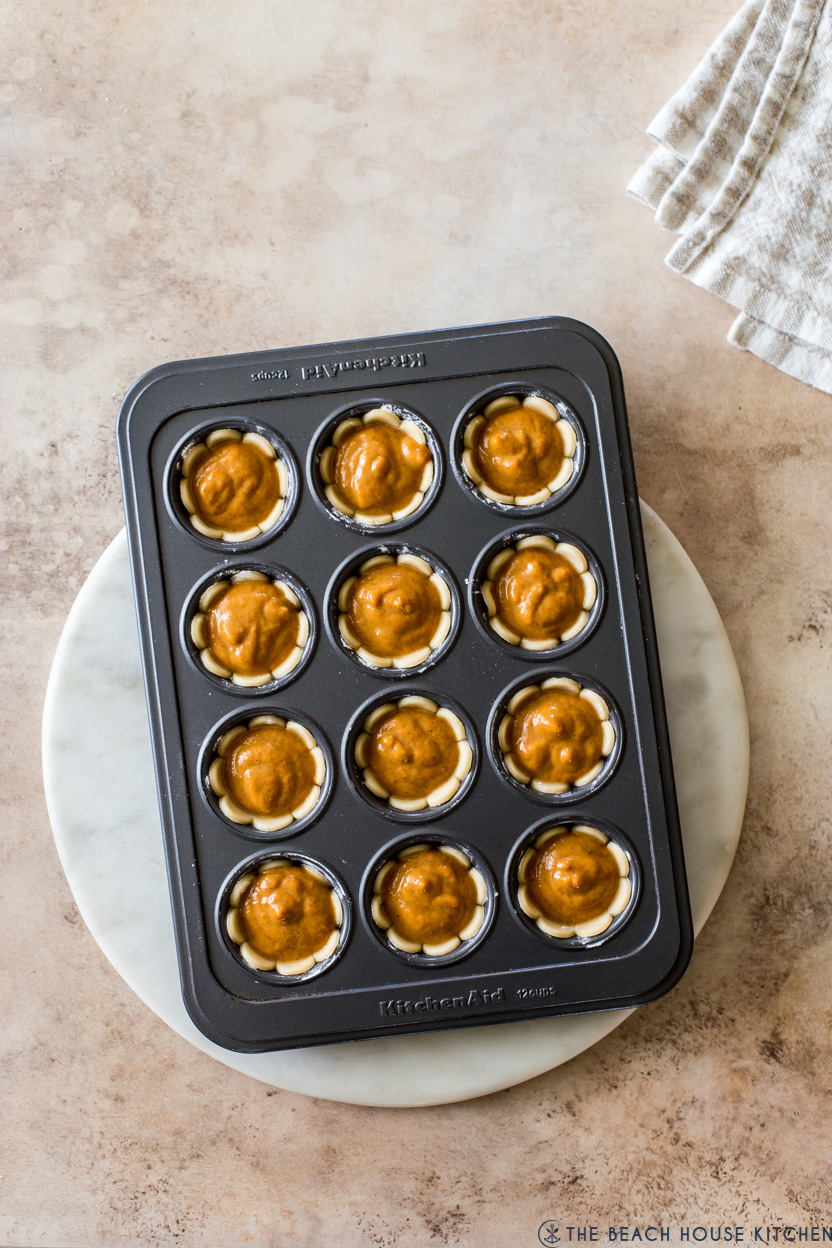 Overhead photo of pre-baked small pumpkin pies in a muffin tin