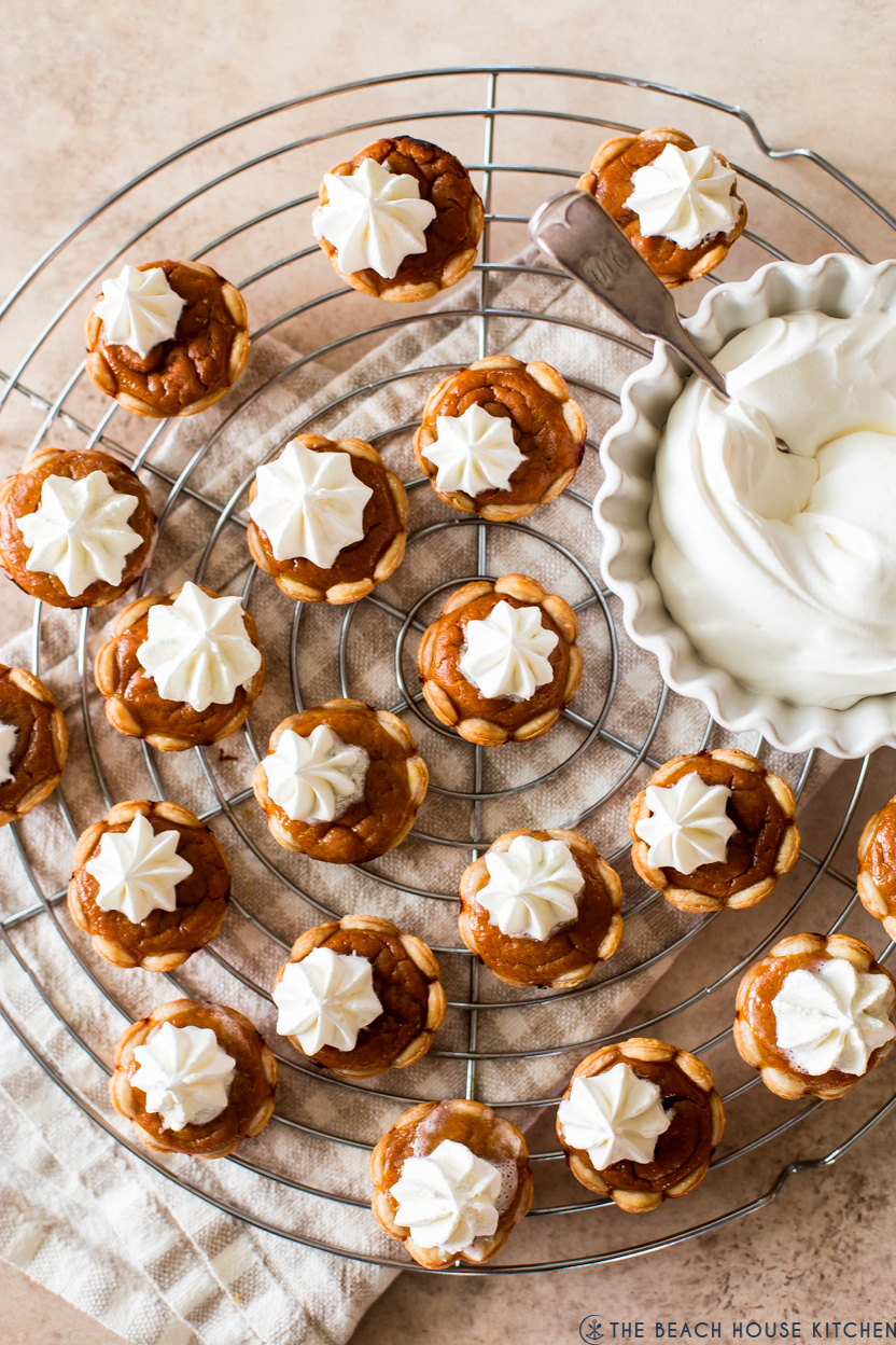 Overhead photo of mini pumpkin pies on a wound wire rack with a small bowl of whipped cream
