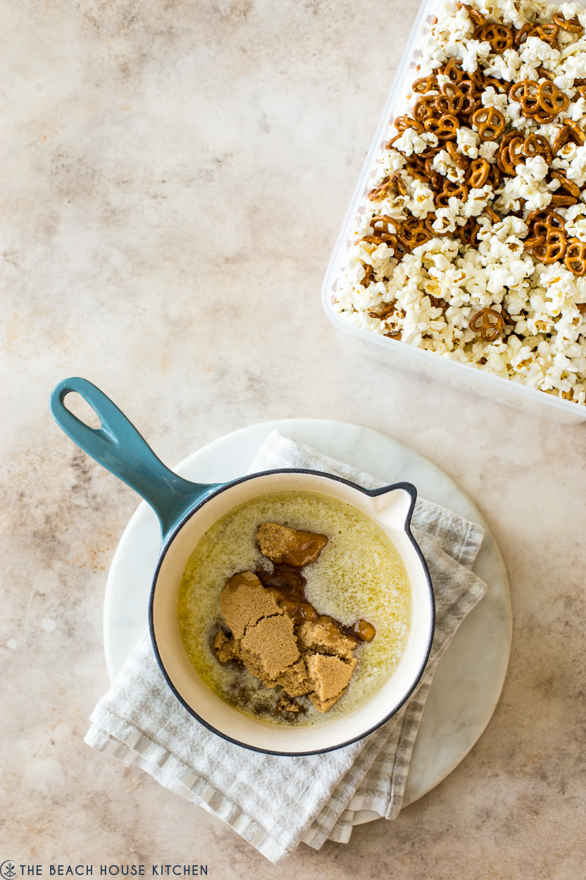 Overhead photo of a pot filled with butter and brown sugar with a container of popcorn and pretzels off to the side,