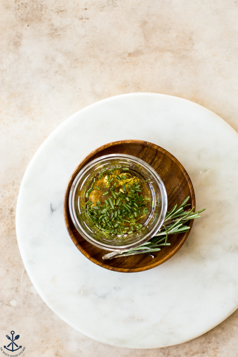 Overhead photo of a glass jar filled with oil and spices on a small round wooden plate