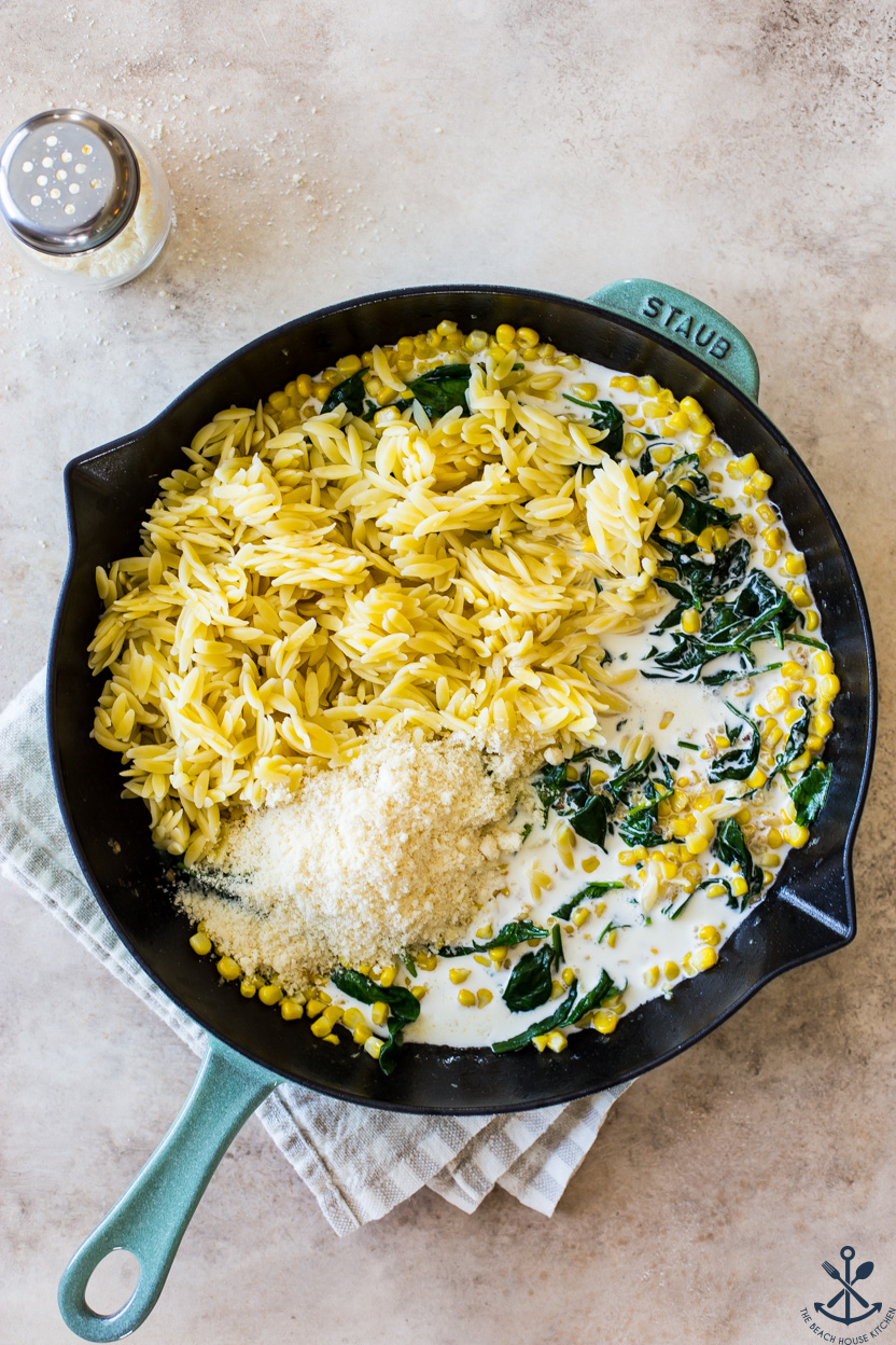 Overhead photo of a skillet of corn, orzo, spinach and grated Parmesan