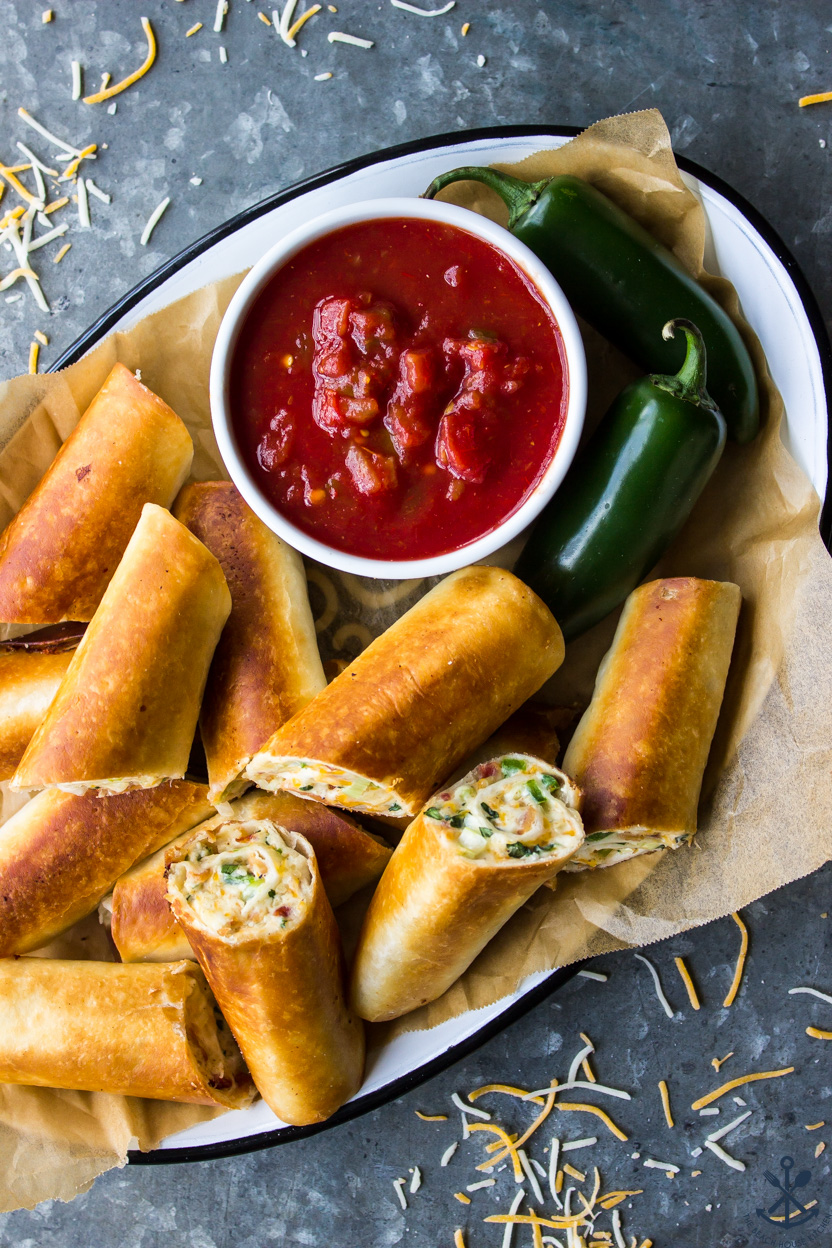 Overhead photo of a platter of Cheesy Bacon Jalapeño Taquitos with a small bowl of salsa