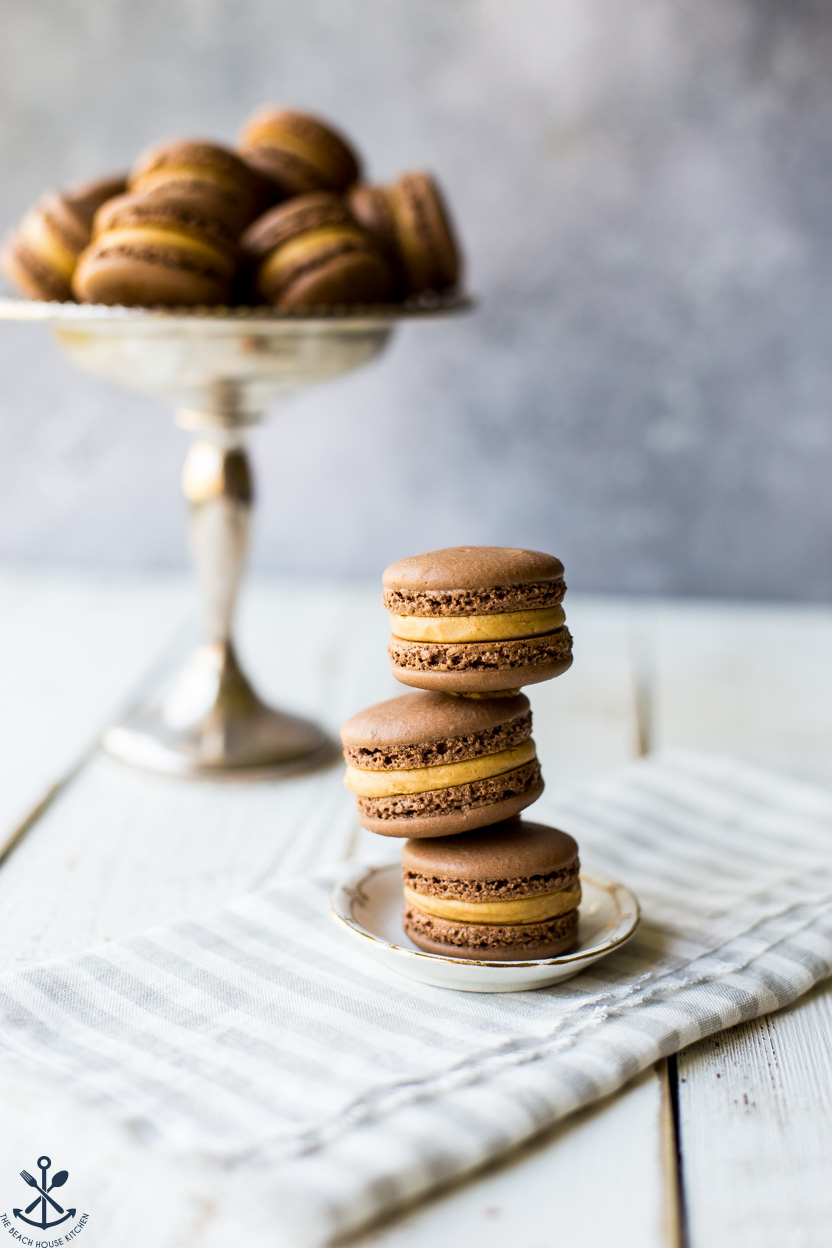 A stack of three chocolate peanut butter macarons on a tiny plate
