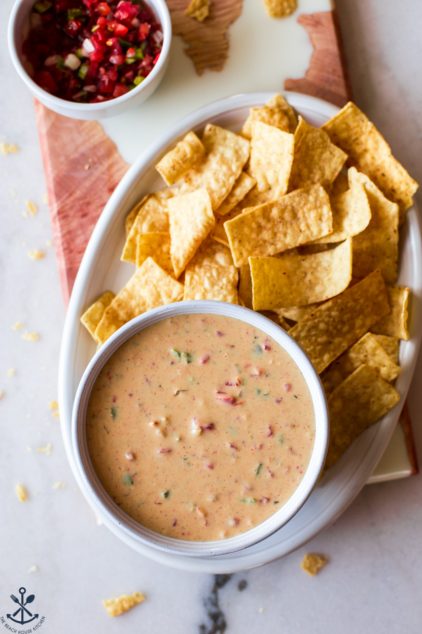 Overhead photo of a bowl of queso on an oval plate with tortilla chips and a bowl of salsa off to the side