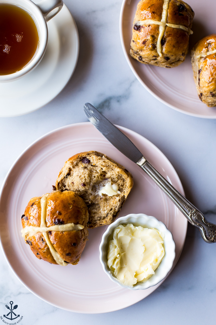 Overhead photo of a hot cross bun on a pink plate with butter
