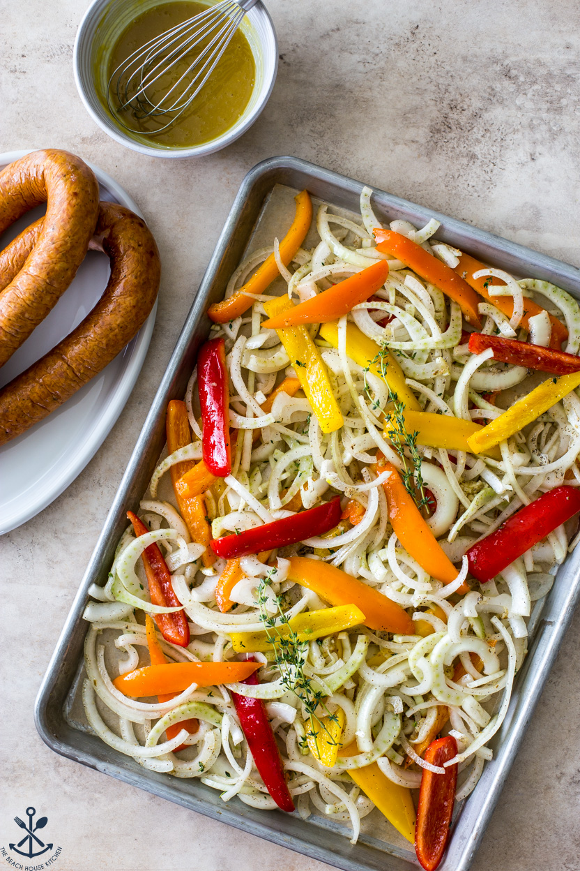 Overhead photo of a sheet pan of onions and peppers with kielbasa rings off to the side