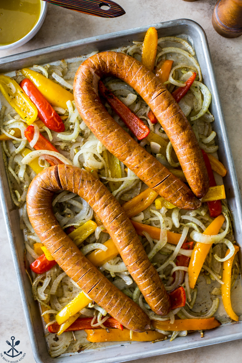 Overhead photo of a tray of pre-cooked kielbasa on top of onions and peppers