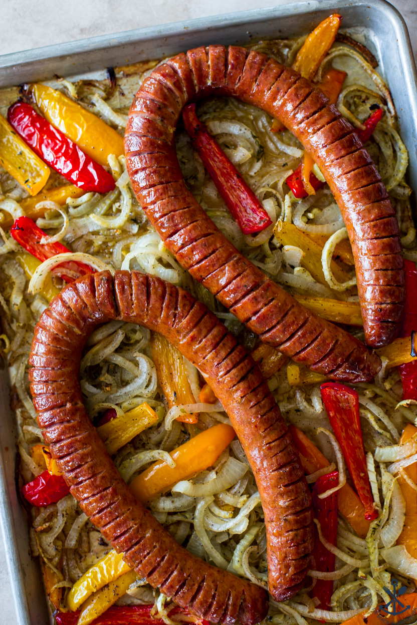 Overhead photo of two rings of kielbasa on a sheet pan atop onions and peppers