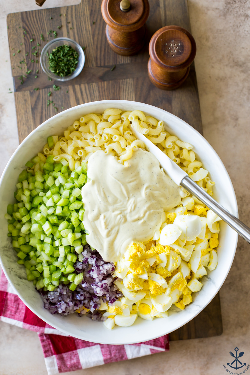 Overhead photo of ingredeints for macaroni salad in a large bowl topped with dressing