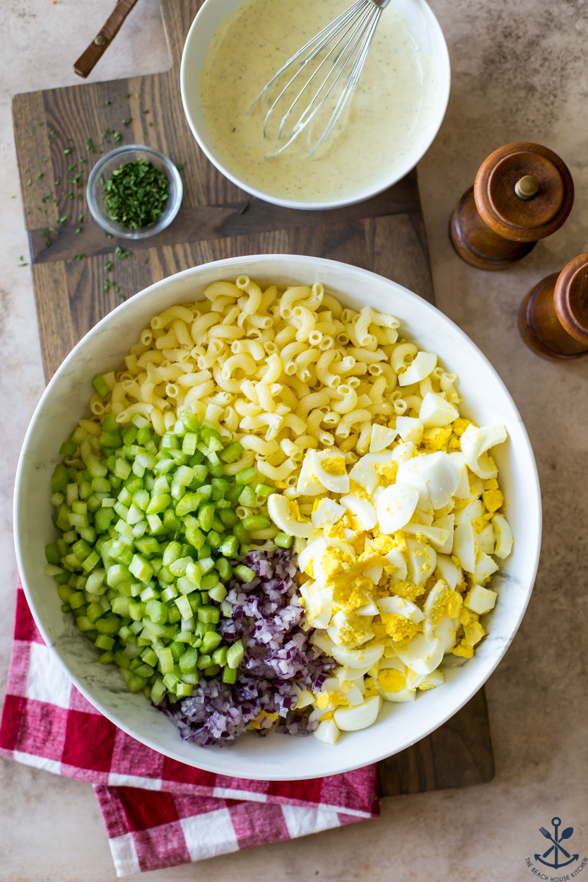 Overhead photo of pre-mixed ingredients for macaroni salad in a white bowl