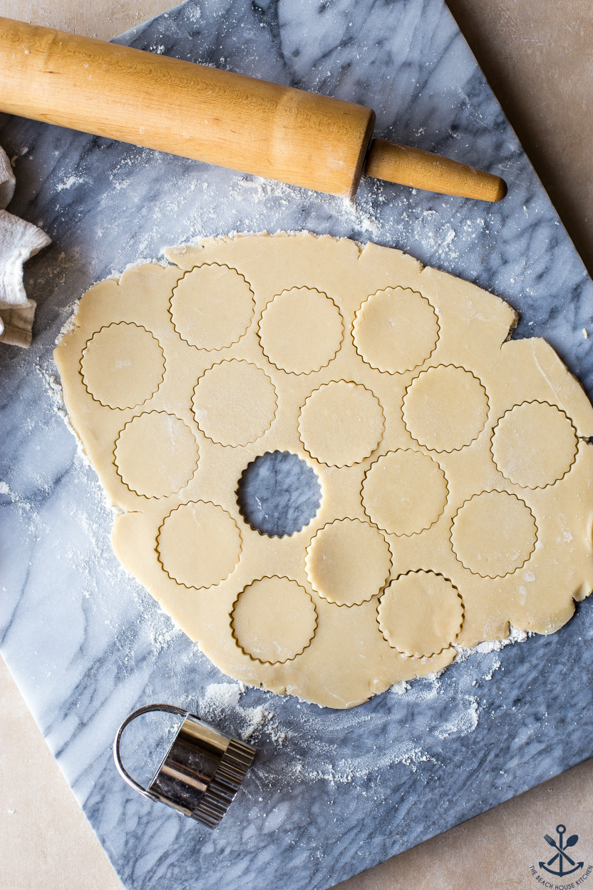 Overhead photo of cookie dough with cut outs and a rolling pin on a marble board