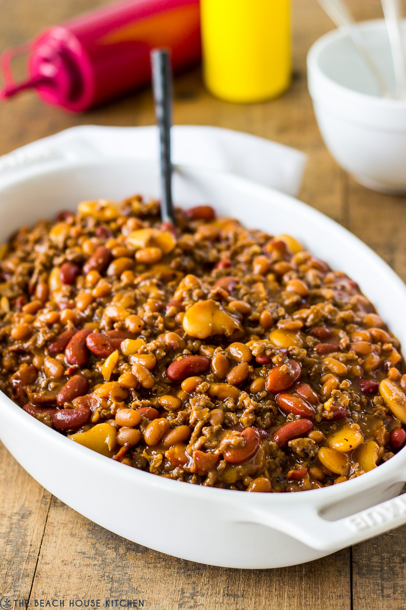 A baked three bean casserole in a white oval dish