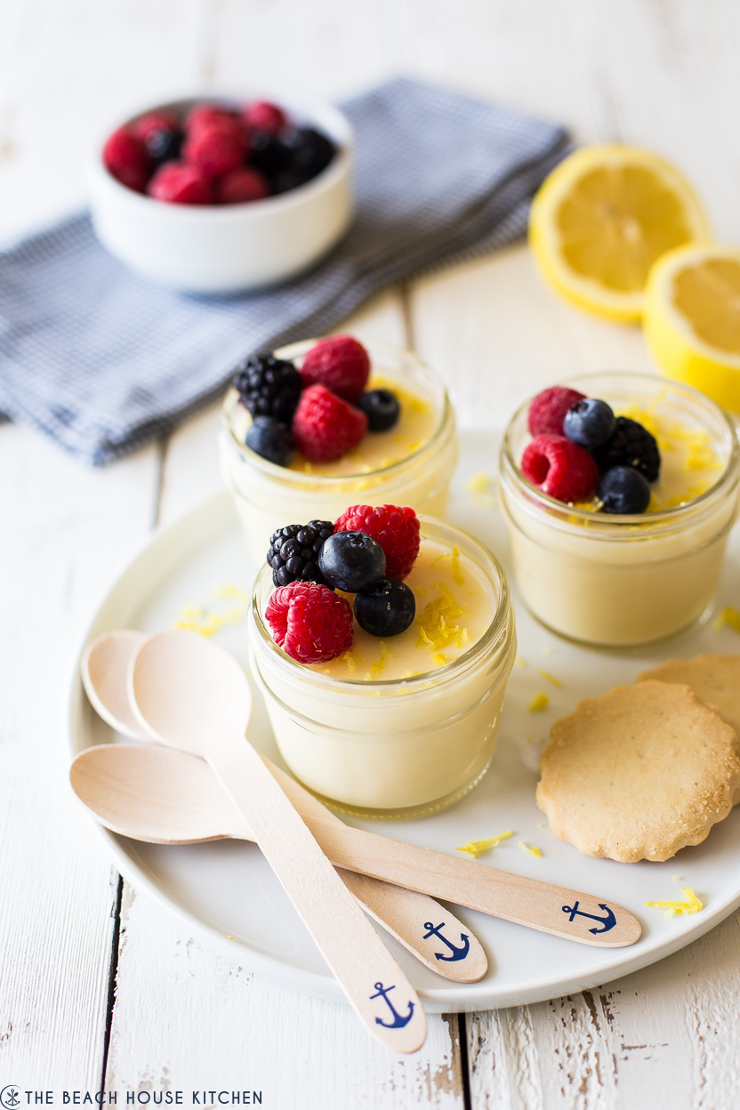 Jars of lemon posset on a plate with spoons and cookies