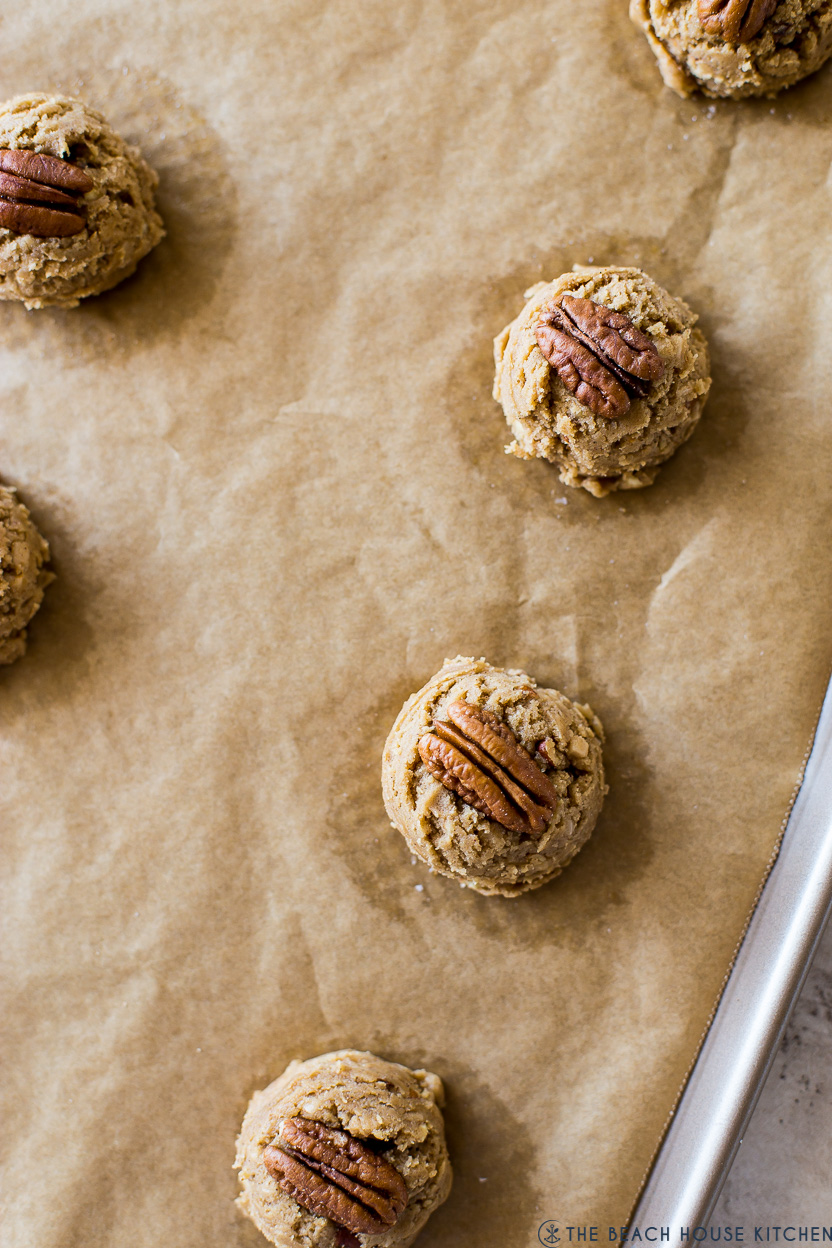 Overhead photo of a baking sheet topped with cookie dough balls topped with pecan halves